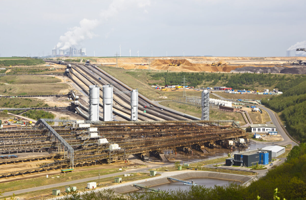 A brown coal pit mine with conveyor belts leading to a distant coal power station.